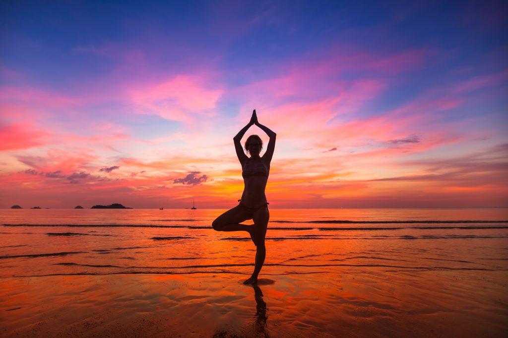 Silhouette of woman practicing yoga during sunset at the seaside